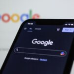 a-close-up-of-a-cell-phone-with-the-google-logo-in-the-background