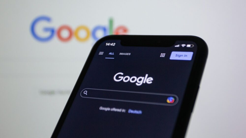 a-close-up-of-a-cell-phone-with-the-google-logo-in-the-background